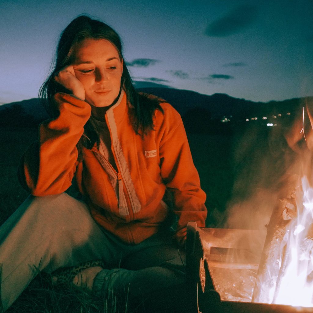 woman looking at campfire with hand on head