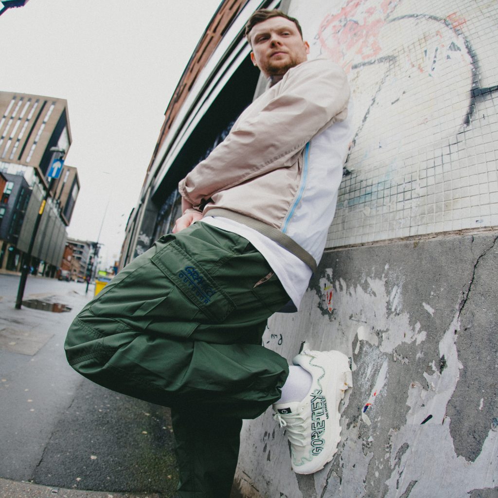 man leaning back against wall with merrell mountain radio trainers
