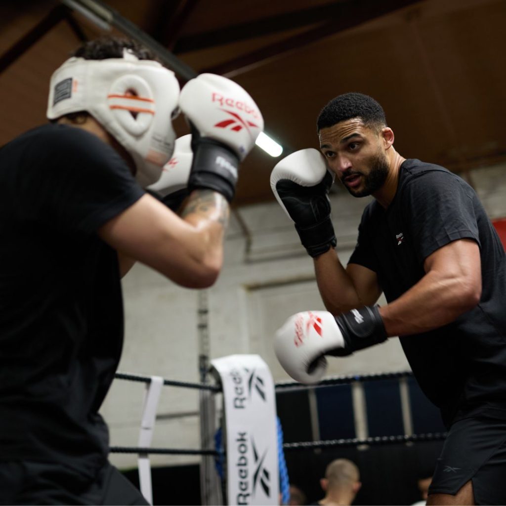 Two men boxing in a boxing ring wearing Reebok boxing gloves.