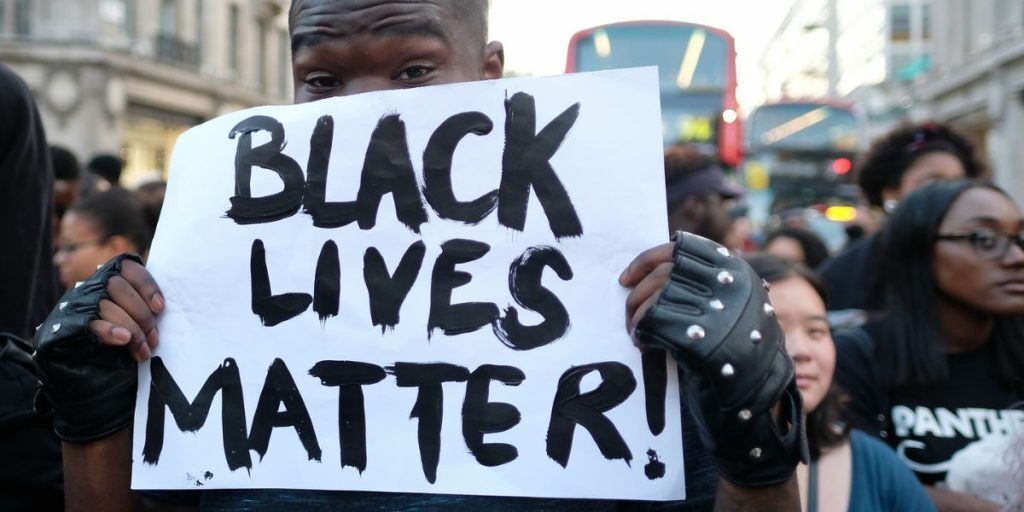 man holding a sign with 'black lives matter' written on it at a london protest