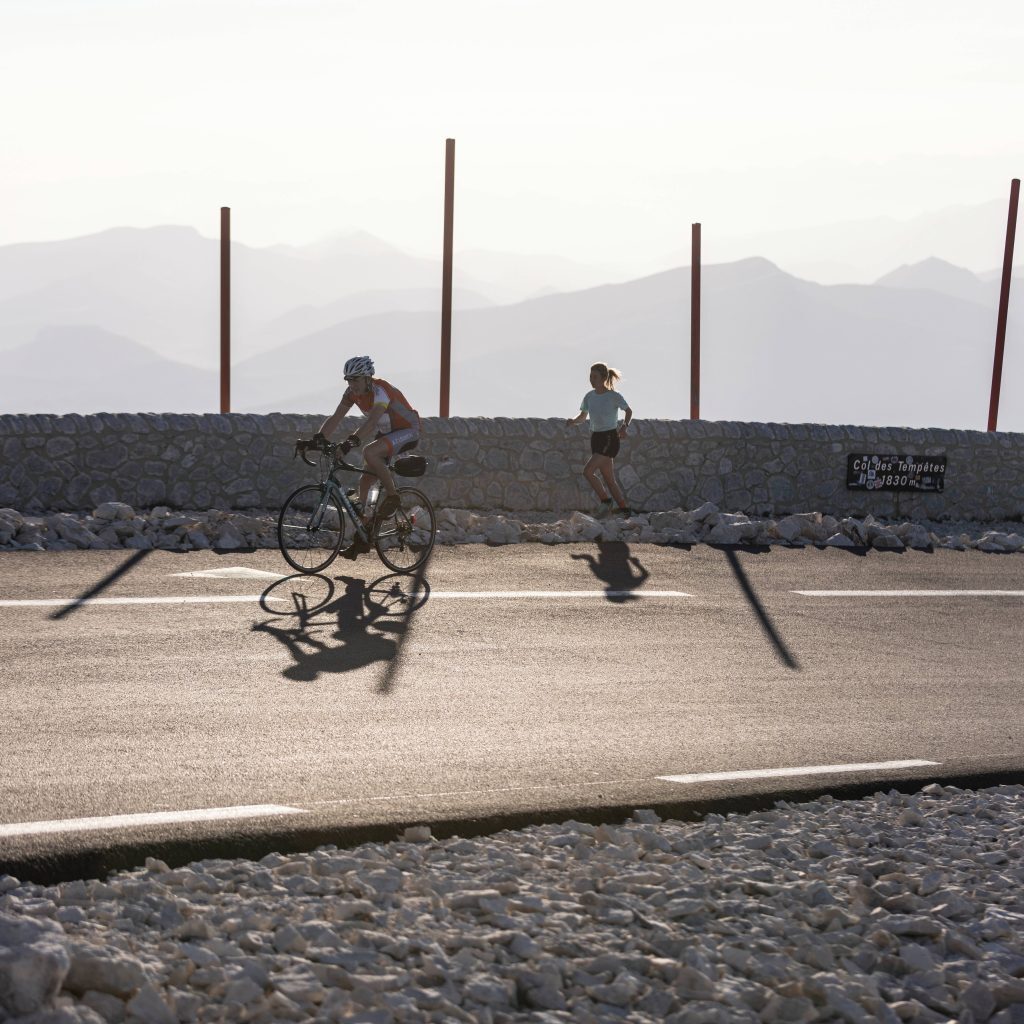cyclist riding bike alongside woman running on bridge