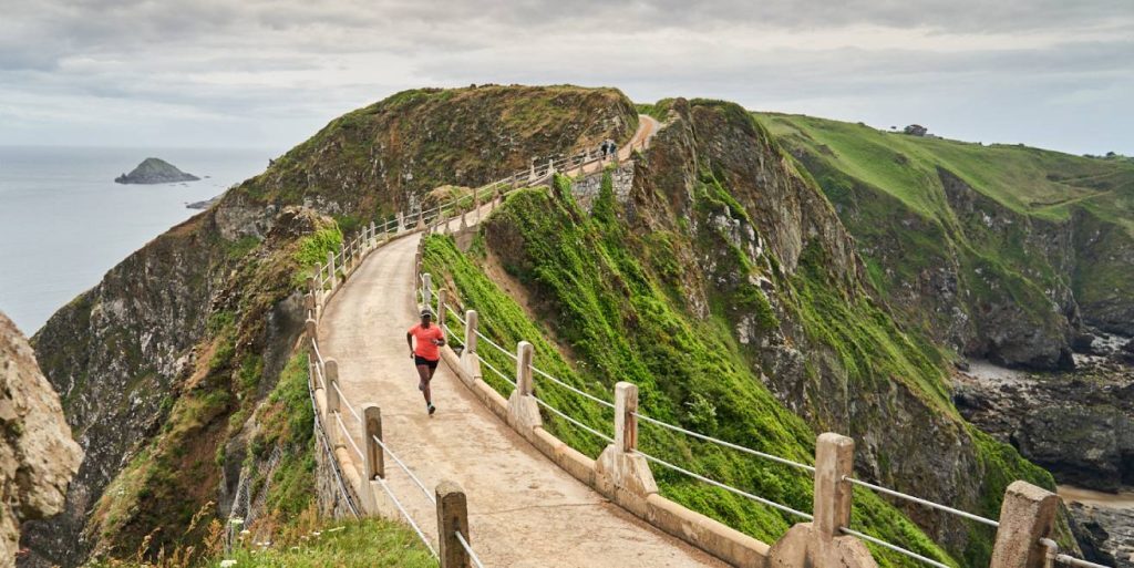 woman running on bridge by the beach wearing merrell trainers