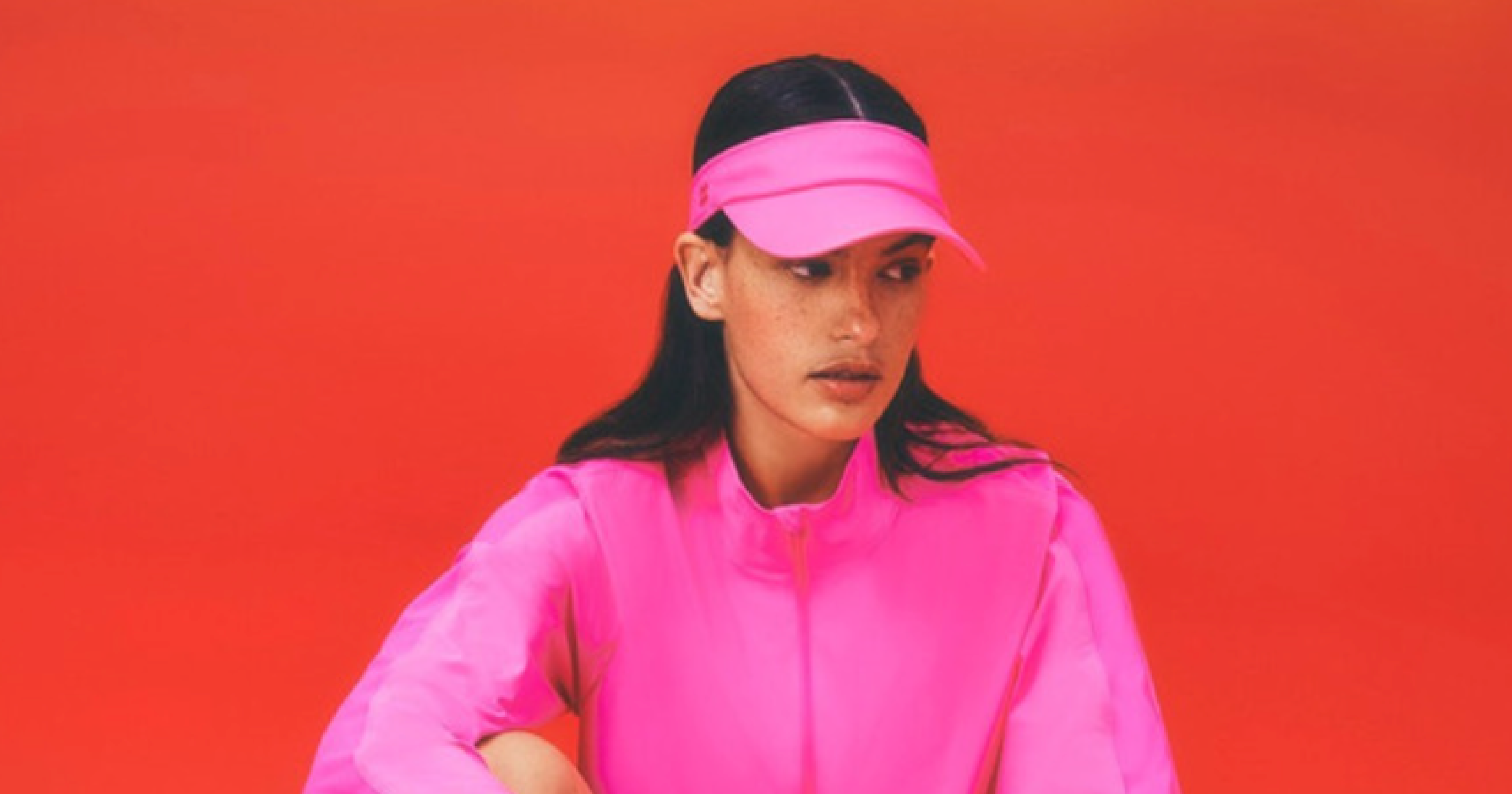 influencer in pink hat and jacket looking to one side with red background