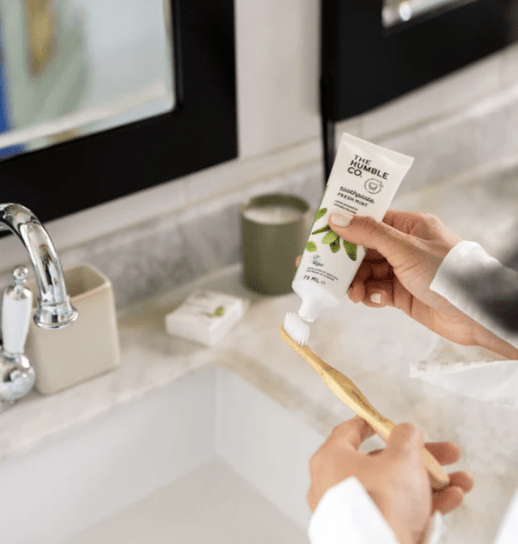 woman applying toothpaste to humble co toothbrush