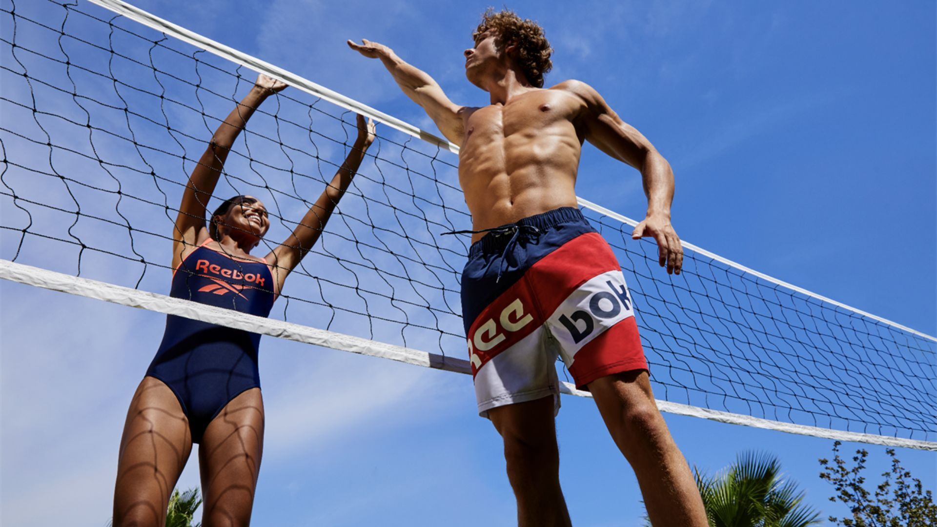 a woman and a man playing volleyball wearing a reebok swim swimming costume and swimming shorts
