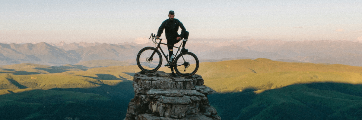 a man stands in front of a mountain view with a bicycle